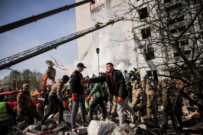 Local residents and rescuers work amidst the rubble at the site of a heavily damaged residential building hit by a missile