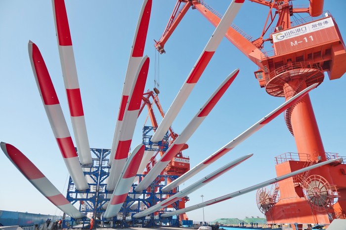 A crane loads red and white wind turbine blades on to a cargo ship in Yantai, China