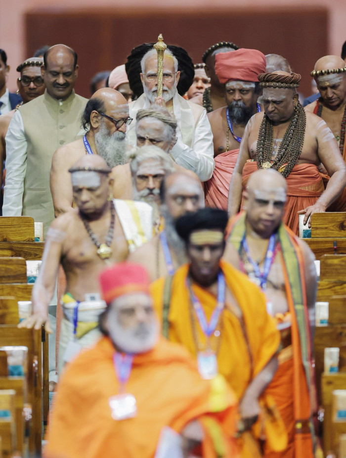 A procession of Indian monks and a man carrying a gold sceptre make their way down an aisle