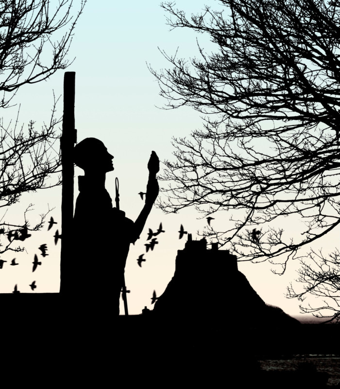 Statue of St Cuthbert in silhouette, with Lindisfarne Castle in the background