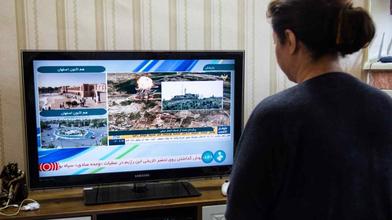 A woman in Tehran watches Iranian news coverage of the explosions