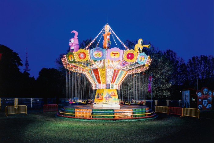 A vibrant merry-go-round decorated with lights and colourful monsters stands in the centre of a field at night