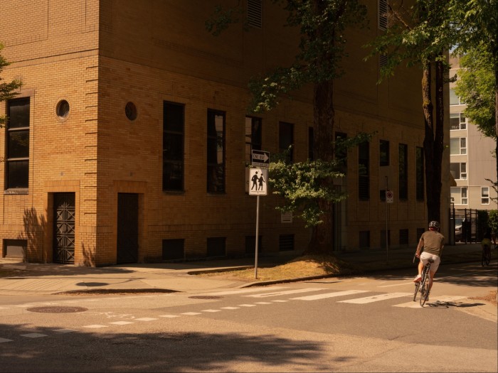 A male cyclist turning a corner on the 10th Avenue route; to his left is a brownstone building