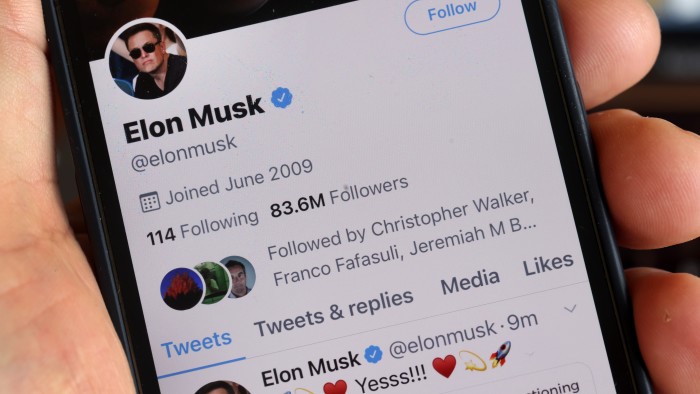 A hand holding a smartphone showing the Twitter page of Elon Musk