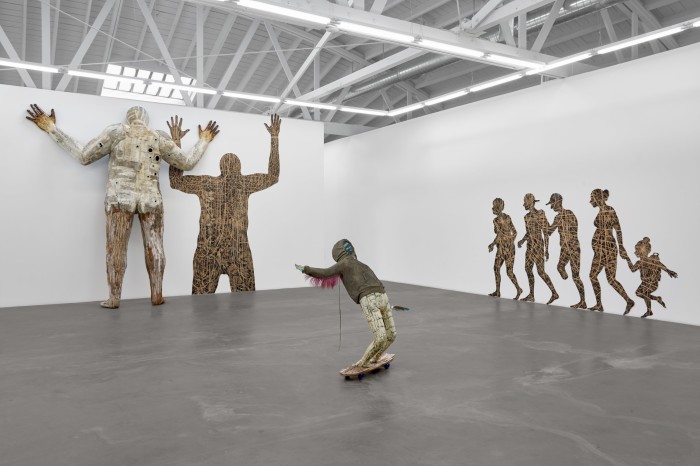 A human-shaped totem stands on the end of a gallery room having the sculpture of a skater at its centre and silhouettes decorating its right-hand side