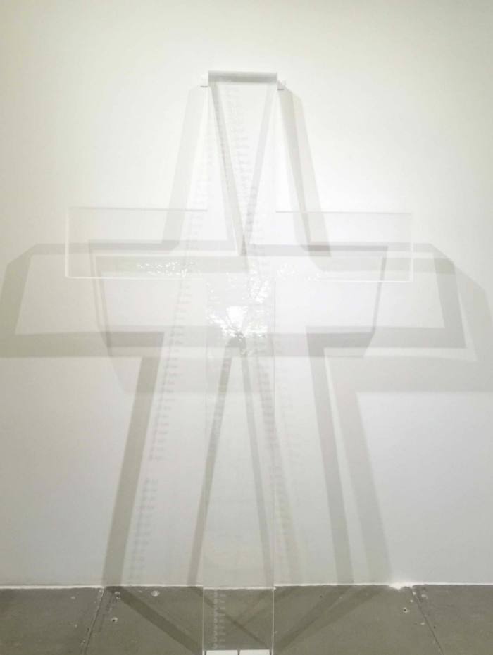  A large, transparent acrylic cross leans against a white wall
