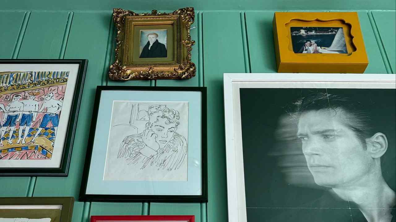 An assortment of various framed pieces of art on a teal wall, ranging from a traditional framed portrait to contemporary posters and drawings, creating a visually stimulating gallery wall