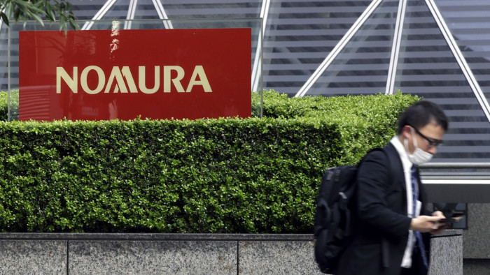 A pedestrian walks past Nomura signage outside its headquarters in Tokyo, Japan