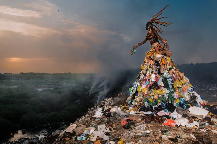 a giant female figure rises up from a mound of refuse: artwork in a dumpsite created using trash