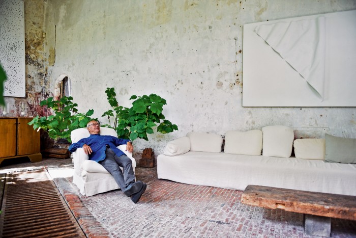 Vervoordt in the Old Orangery, one of his favourite rooms in the  outer buildings of ‘s-Gravenwezel, his and his wife May’s 12th-century castle near Antwerp. Vervoordt designed the table from an old piece of wood. The painting above the sofa is by Japanese Gutai artist Norio Imai