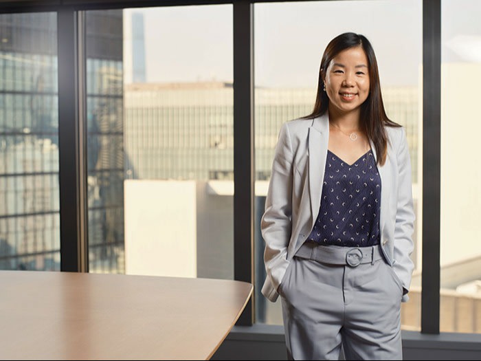 Jocelyn Tsao, wearing a suit, stands beside an office table, her hands in her trouser pockets