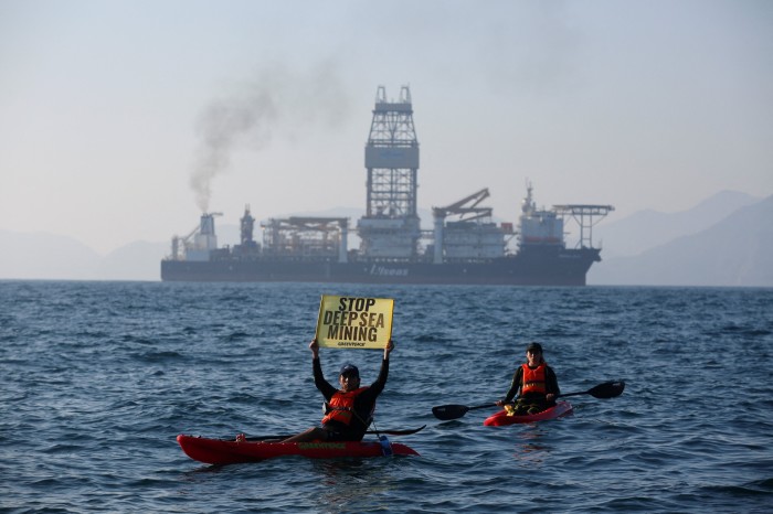 Two people on kayaks with a ship in the background. One of the persons is holding a sign that says ‘Stop Deep Sea Mining, Greenpeace’