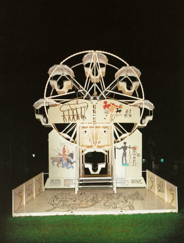 A Ferris wheel stands in the centre of a vertical night shot, covered in stylised graffiti of human figures