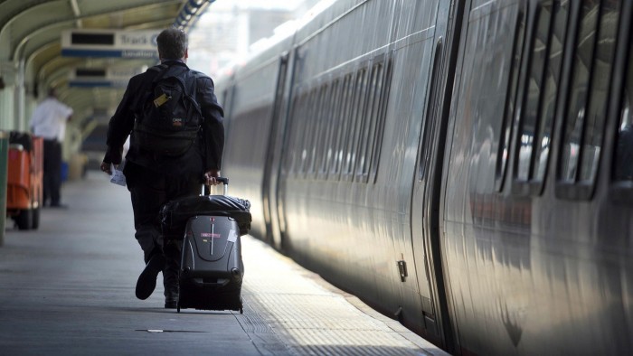 A lone passenger wheels a suitcase alongside a train, stopped in a platform