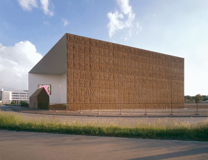 A large box of a building, with one side visible which looks like roughly patterned clay