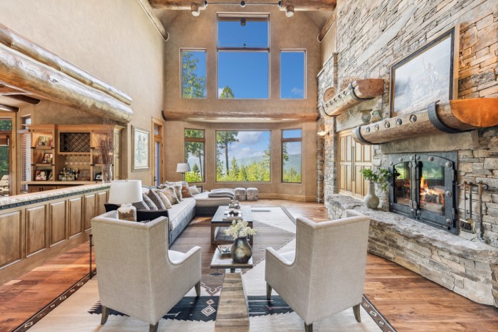 A large living area with a stone fireplace and double-height windows looking out on woodland and blue sky