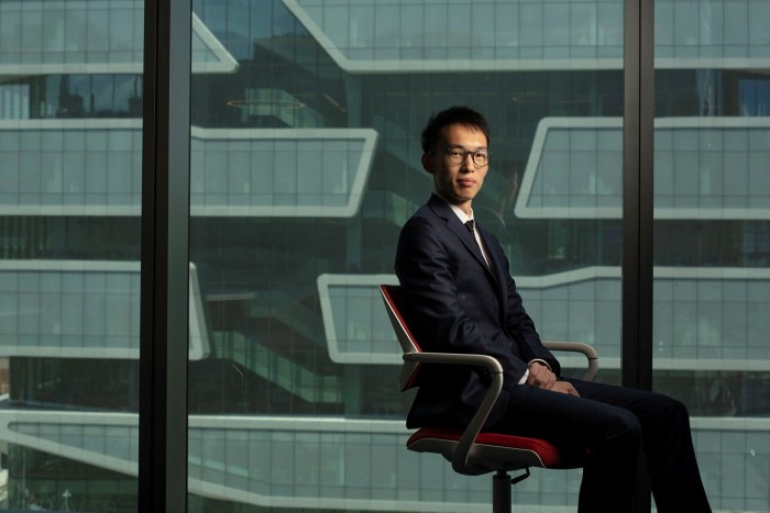 Columbia Business School masters graduate Kevin Guo.  A young man sitting on an office chair next to the glass walls of a building