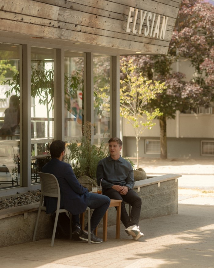Two men sitting at a table outside a branch of Elysian Coffee Roasters