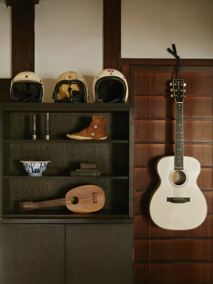 Pieces from his archive on a cabinet: vintage motorcycle helmets, a moccasin, bowl, ukulele and guitar