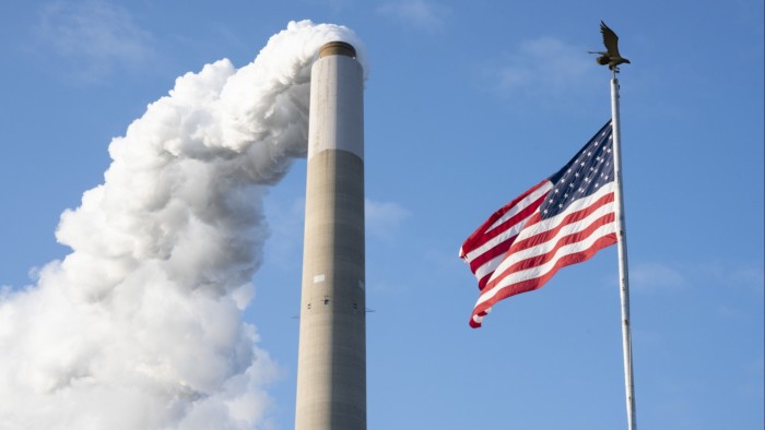 Emissions rise from a smokestack alongside an American Flag in