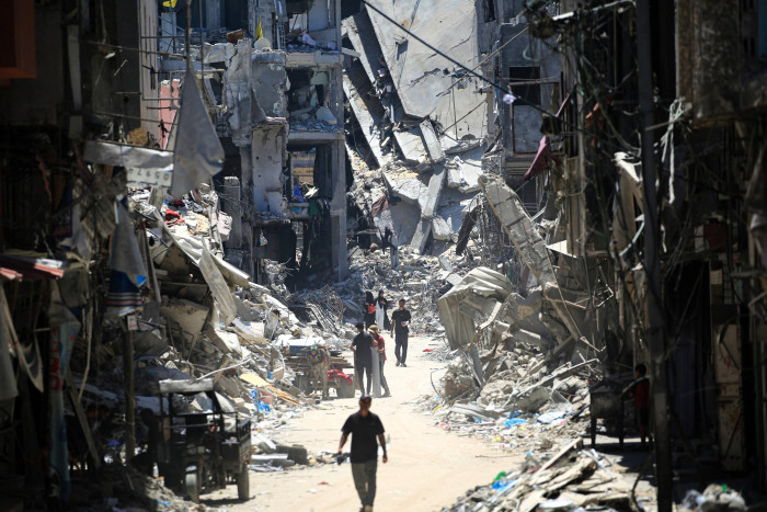 Palestinian men walk between destroyed buildings in Khan Yunis in Gaza