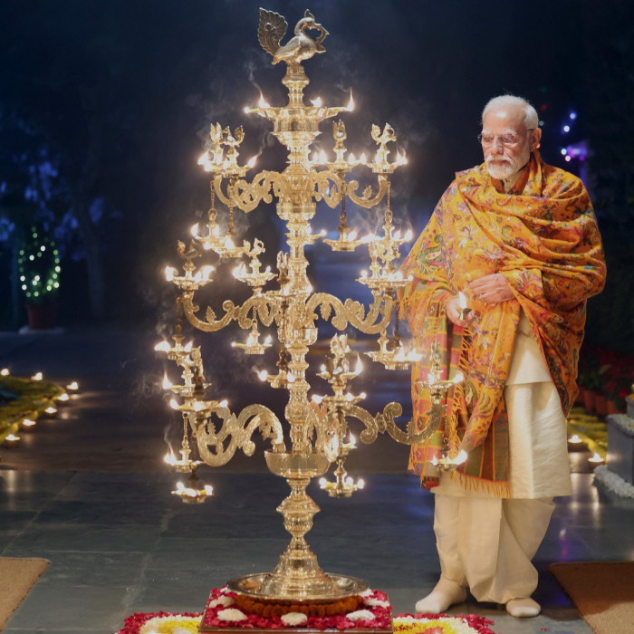 A man dressed in an orange kurta lights some candles on a golden tree