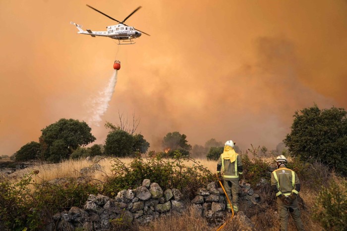 A helicopter drops water as fires rage in Navalmoral de la Sierra near Avila at center of Spain