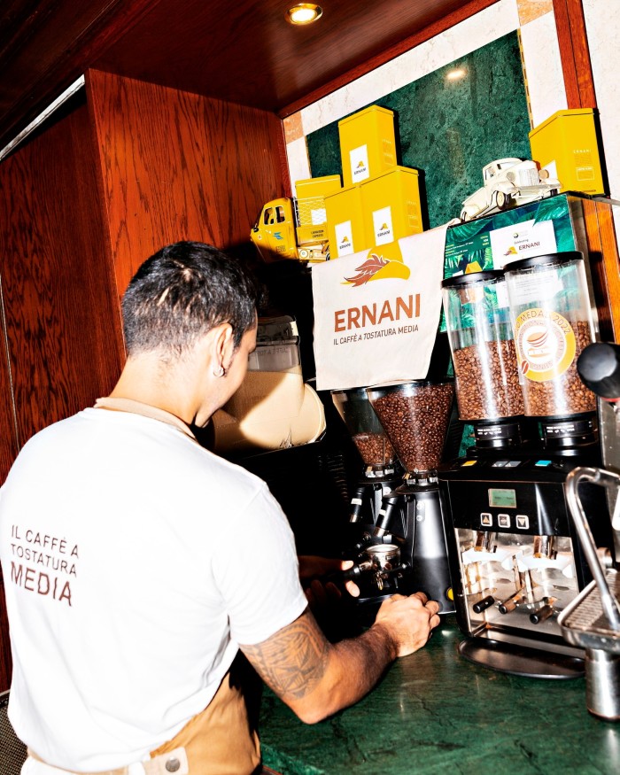 A male barista with tattooed arms grinding coffee on a green-marble counter at Torrefazione Ernani