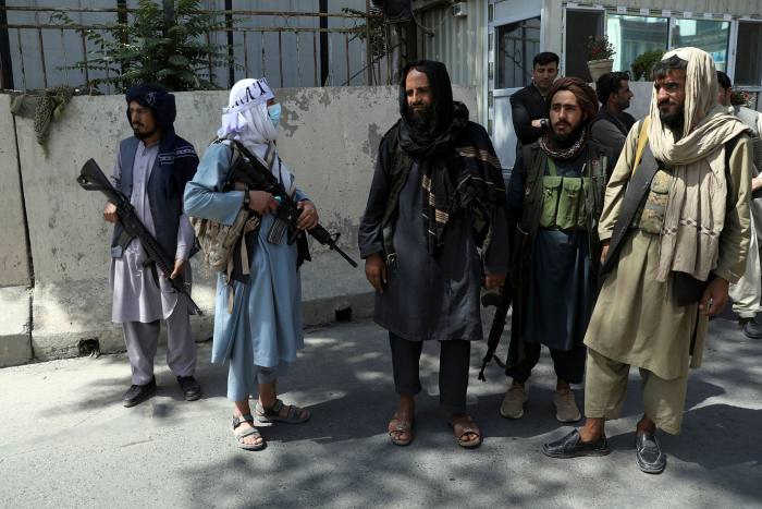 Taliban fighters stand guard at the main gate leading to the presidential palace on August 16