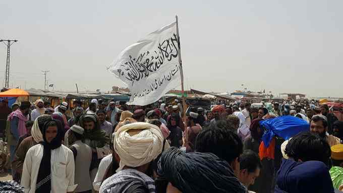 People gather around a Taliban flag as they wait for relatives to be released from jail
