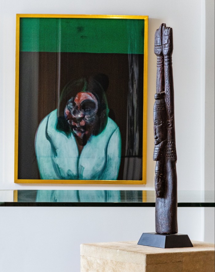 Painting of a woman with a swirling face behind a tall thin wood statue
