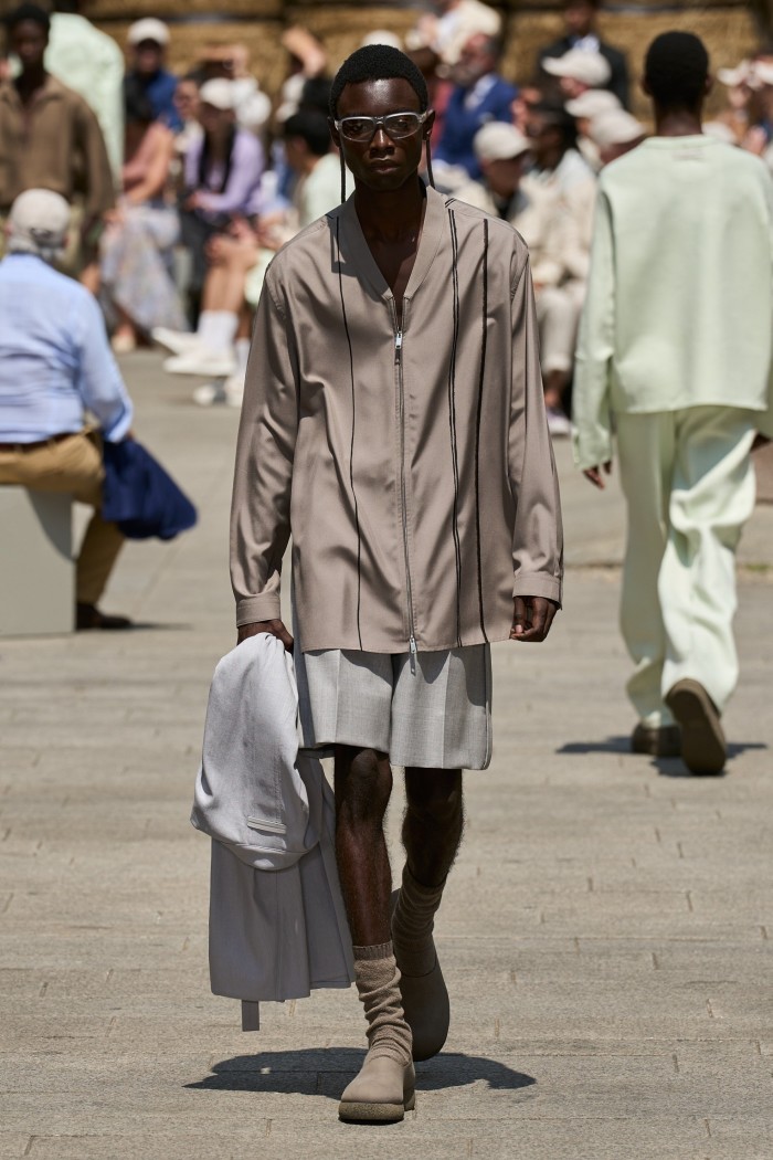A model in shorts, beige ankle books and taupe coloured zip-front shirt