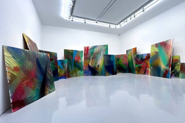 A series of large, colourful abstract canvases lean against the walls of an entirely white gallery space 