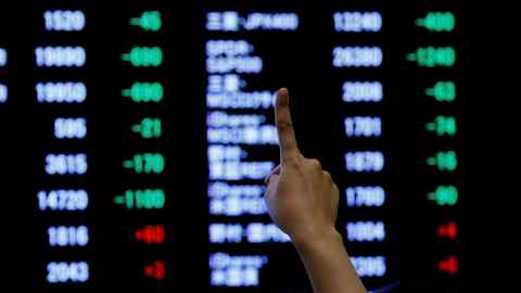 A woman points to an electronic board showing stock prices