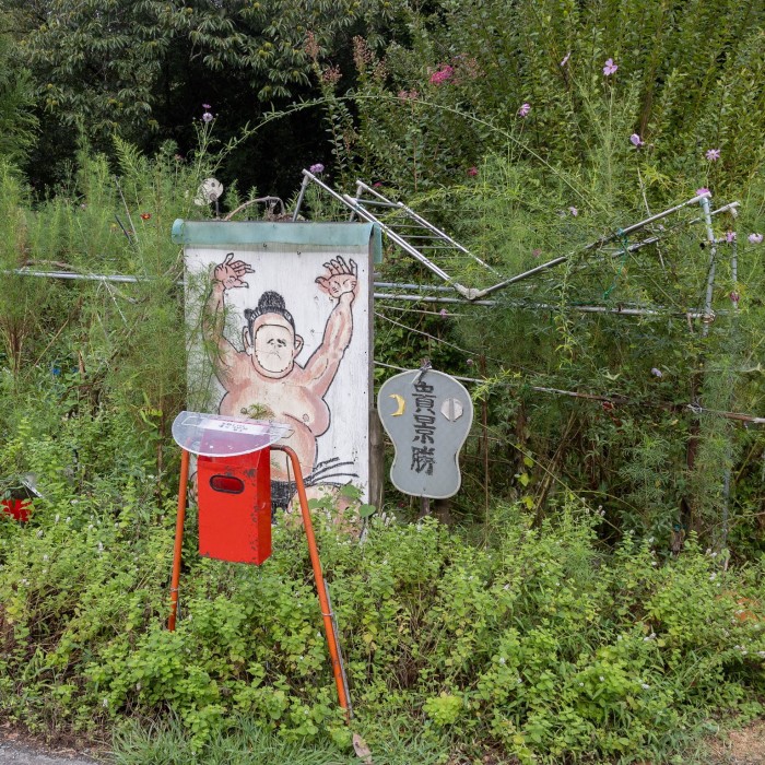 A picture of a sumo wrestler painted on a panel at the entrance to a garden plot