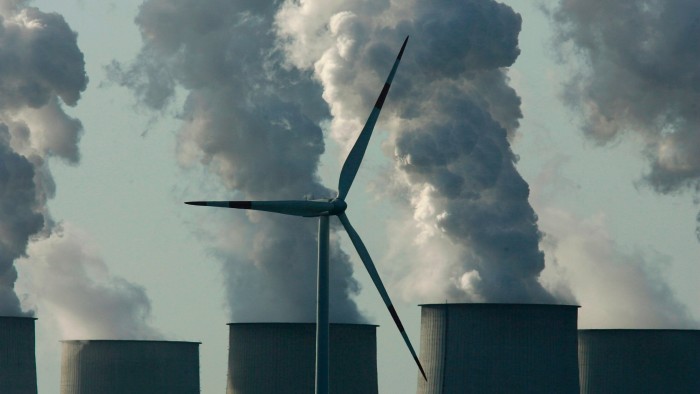A lone wind turbine spins as smoke plumes from power station cooling towers 