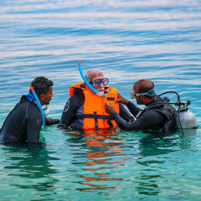 Three men wear snorkelling gear while standing in the sea