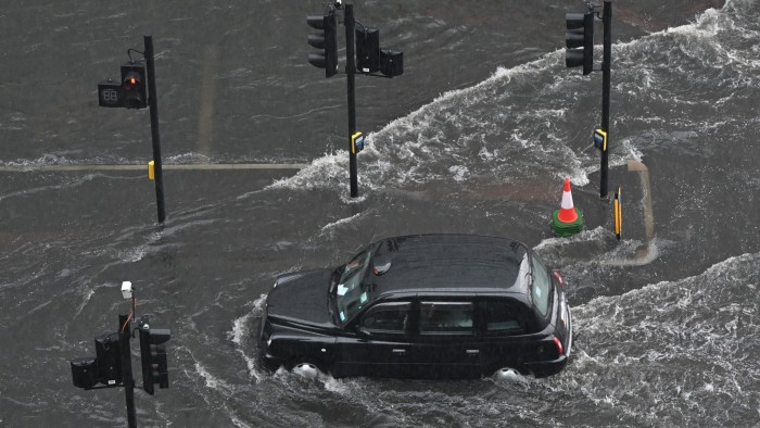 A London taxi drives through water on a flooded road in The Nine Elms district of London