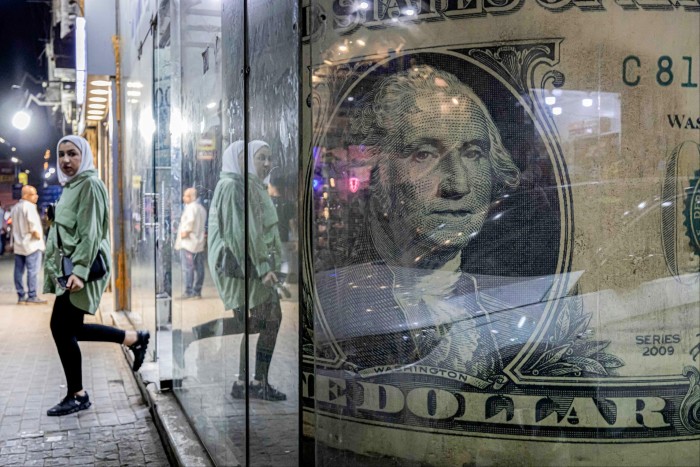 A woman walks out of a currency exchange shop displaying a giant US dollar banknote