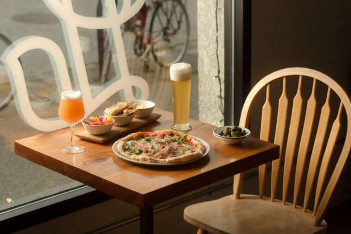 A pizza from the brewery’s in-house pizzeria on a table, alongside two different glasses of beer