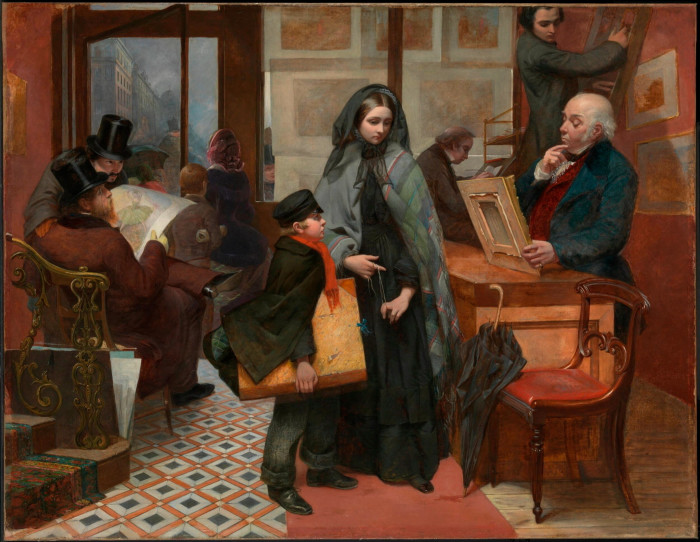 In a gallery where there are pictures on the walls, a Victorian woman and a young boy stand near a counter where a man inspects a painting