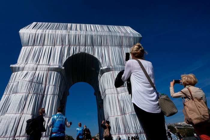 People taking photos of a large arch wrapped in white fabric