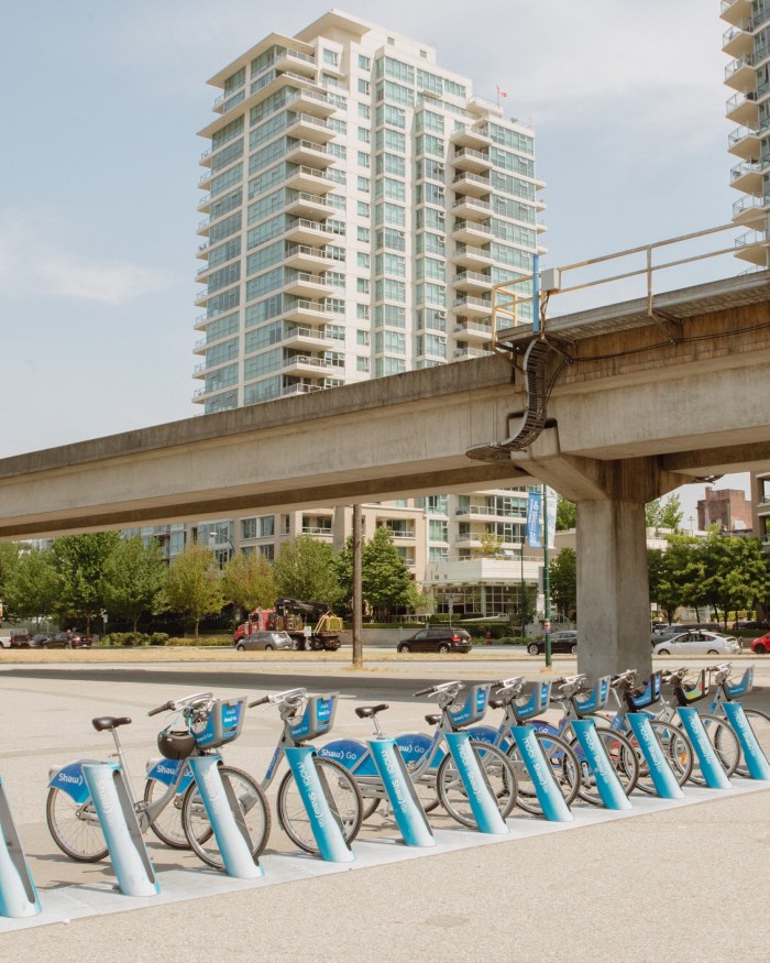 Blue bicycles in one of the 240-plus stations in the city’s Mobi by Shaw Go bike-share scheme, in front of a concrete bridge and high-rise apartment blocks