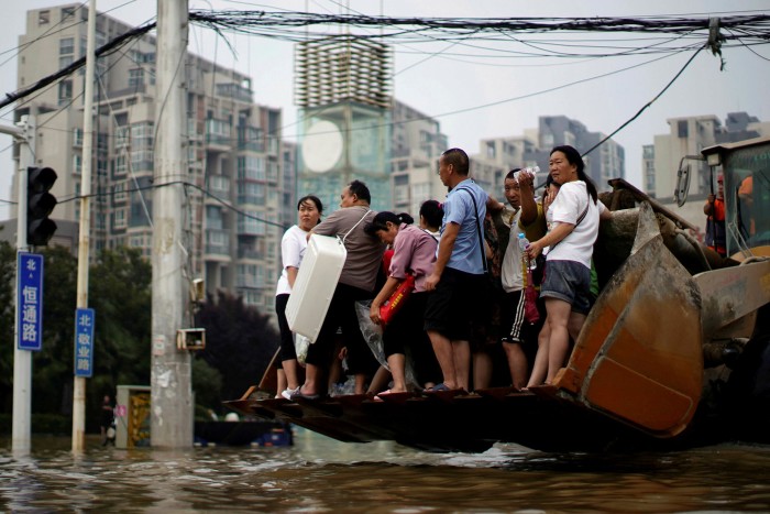 People ride on a front loader as they make their way through floodwaters