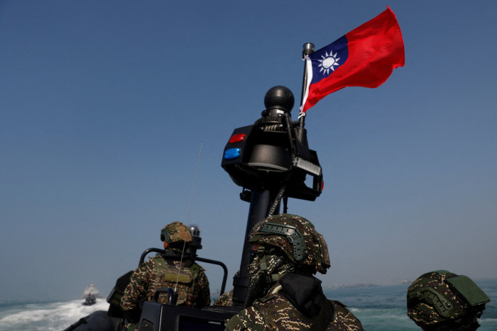 Men in combat gear stand on a boat near a Taiwanese flag that is fluttering in the breeze