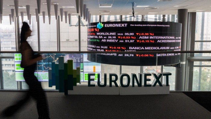 A person walks past stock price information above a trading floor at the Euronext stock exchange in Paris