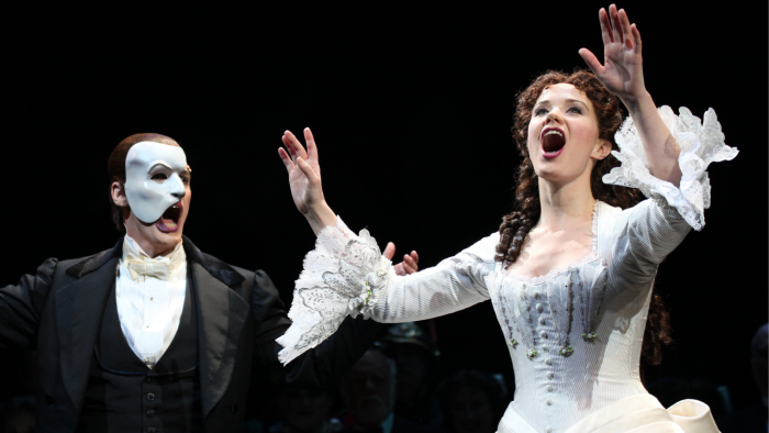 Hugh Panaro (dressed in black cape and white mask) and Sierra Bogges (in a white dress) sing on stage