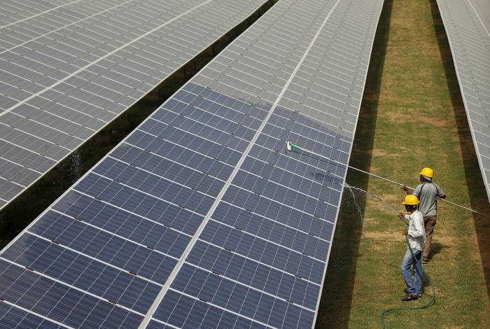 Workers clean photovoltaic panels inside a solar power plant in Gujarat, India