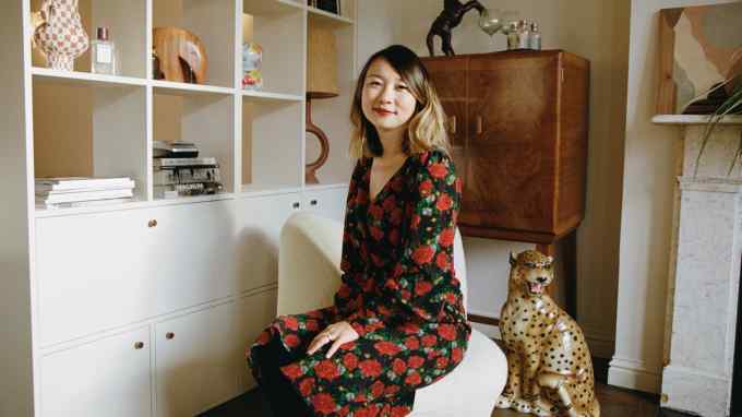 A smiling woman sits on cream-coloured fabric chair with a mahogany chest behind her and a porcelain leopard at her side