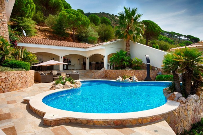 A view across a pool to a traditionally styled Spanish home with whitewashed walls, archways and terracotta-red roof tiles